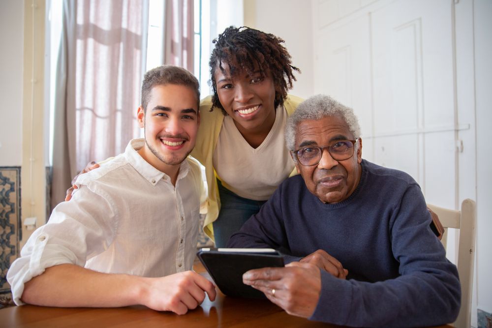 A young man, a woman and an older man smiling together around a table