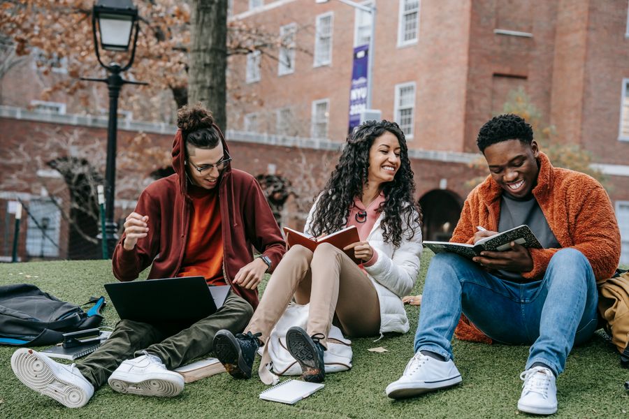 Three friends laughing and studying together on a lawn